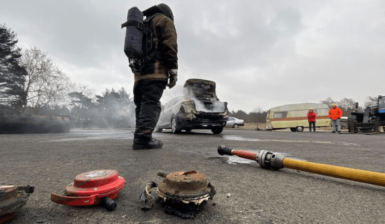  A firefighter stands beside the smoking EV after the Fire Isolator equipment has been deployed in action.