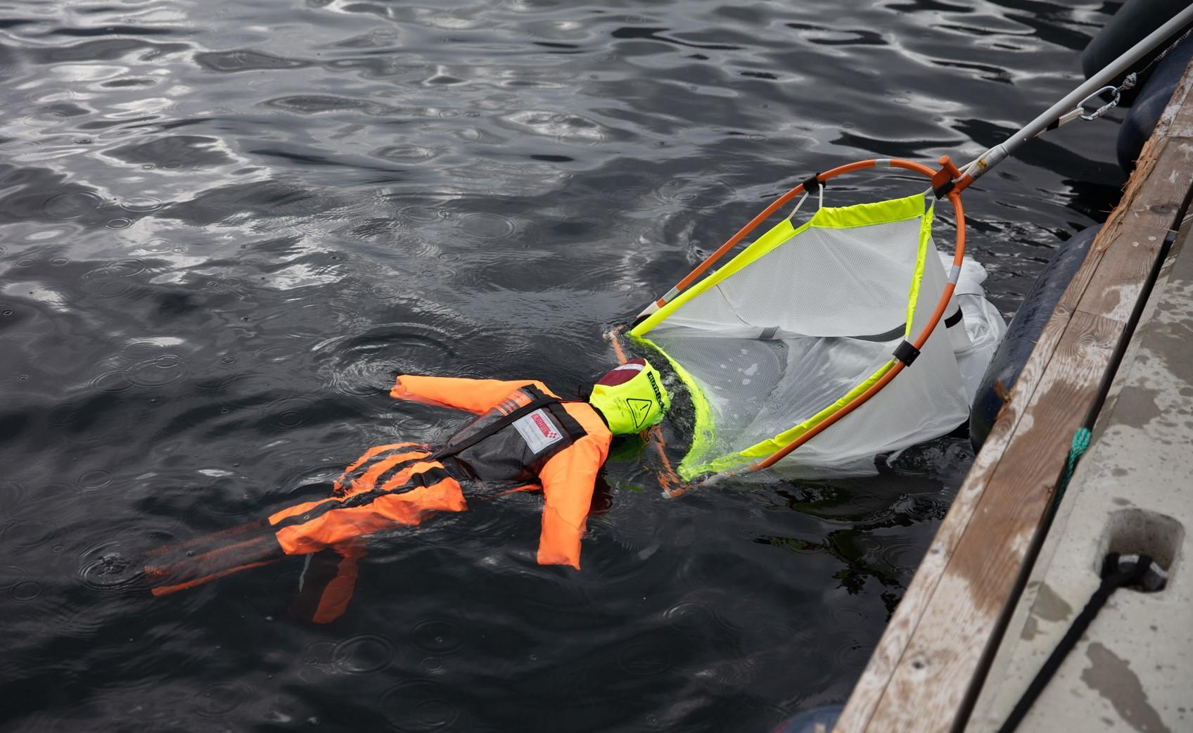 Orange Man Overboard Manikin guided into SB Rescue Sling net near the side of the rescuing vessel.