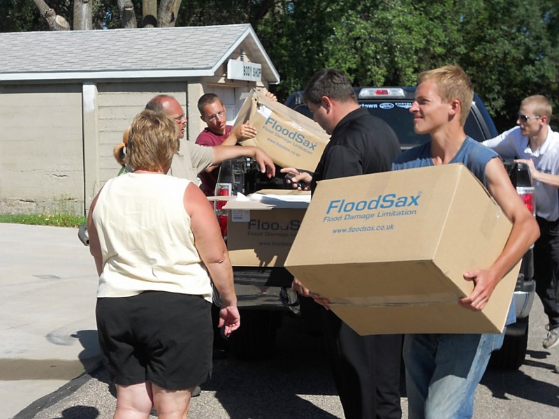 Cardboard boxes of FloodSax being carried by people to provide local populations with efficient and portable flood defense solutions.