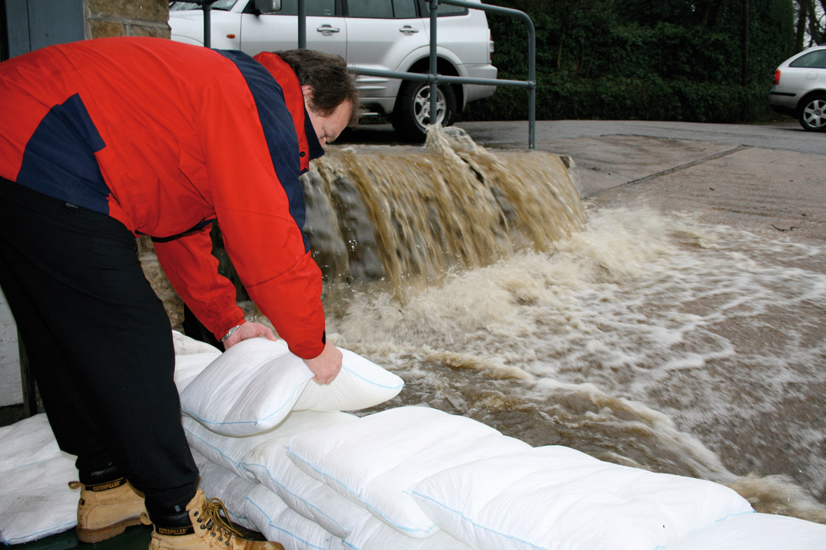  A man constructs a flood barrier using FloodSax flood defense bags to contain flooding.